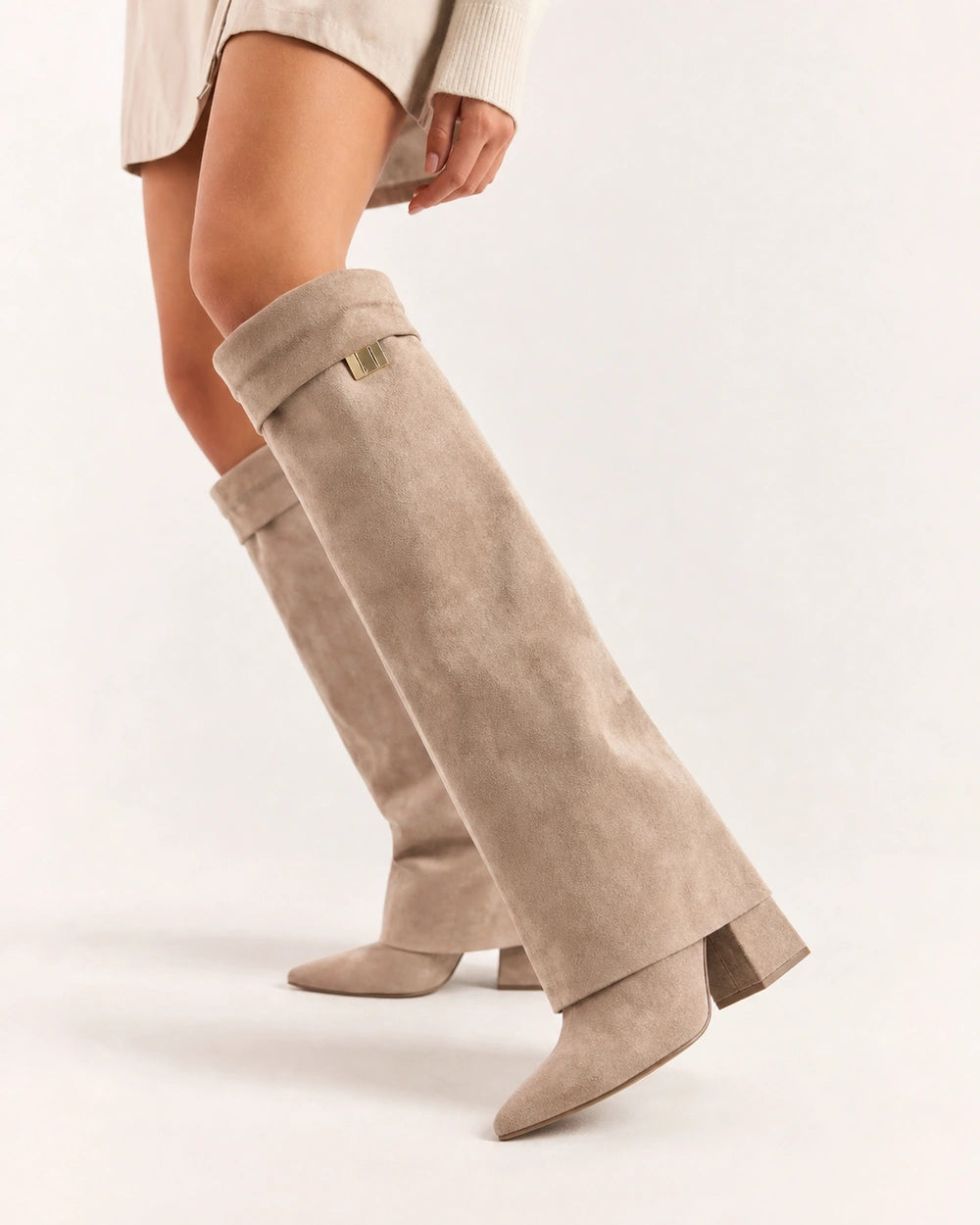 Beige suede-effect knee-high boot showing the folded cuff, small gold badge, pointed toe and block heel.